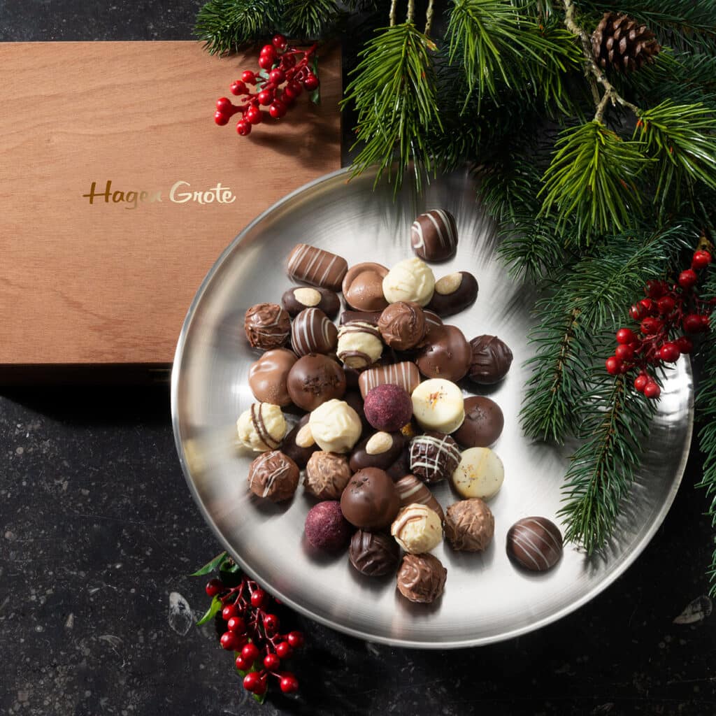 Edle Pralinenmischung auf Silberplatte mit hölzerner Hagen Grote Box und Tannenzweigen.