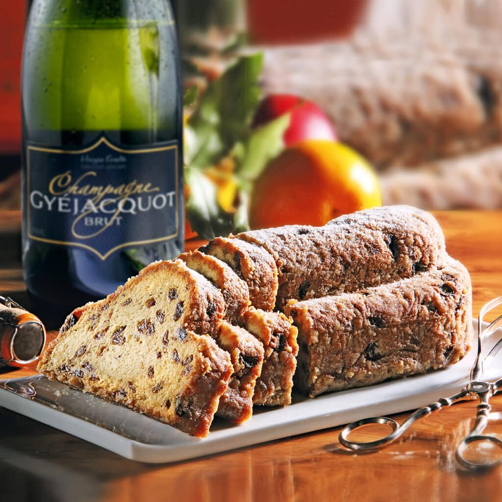 Aufgeschnittener Rosinenstollen auf Platte neben Champagnerflasche.