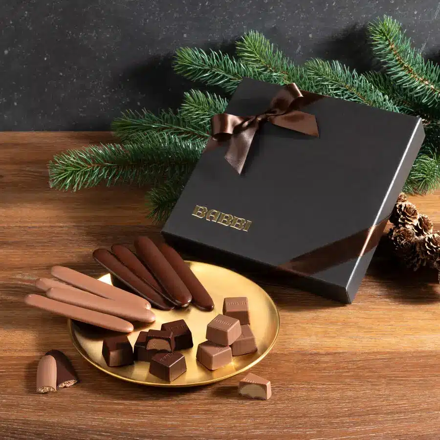 Elegante Babbi-Schokoladen-Geschenkbox mit Trüffelstangen und Pralinen, festlich dekoriert mit Tannenzweigen