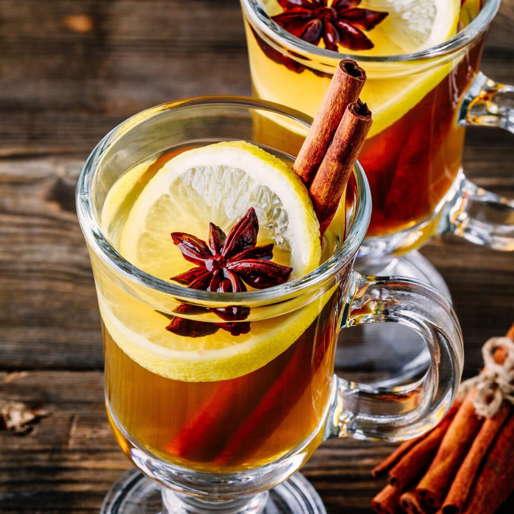 Heiße Tasse Glühwein mit Zitrone, Zimtstange und Sternanis auf rustikalem Holztisch