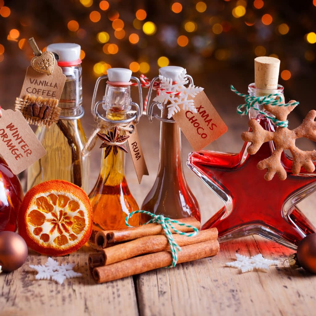 Verschiedene hausgemachte Weihnachtsliköre in dekorativen Flaschen mit Zimt und Orangen