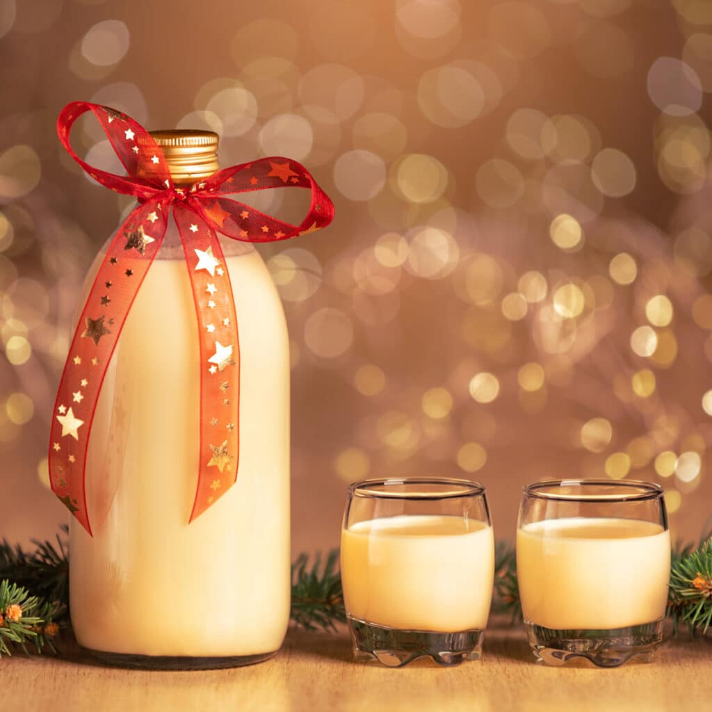 Flasche Eierlikör mit roter Schleife und zwei Gläsern vor goldenem Bokeh-Hintergrund