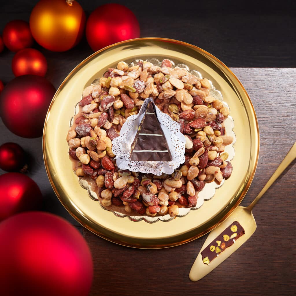 Nusskrokant-Kranz mit Mandeln, Pistazien und Schokolade in Pyramidenform, festliche Präsentation mit roten Weihnachtskugeln.