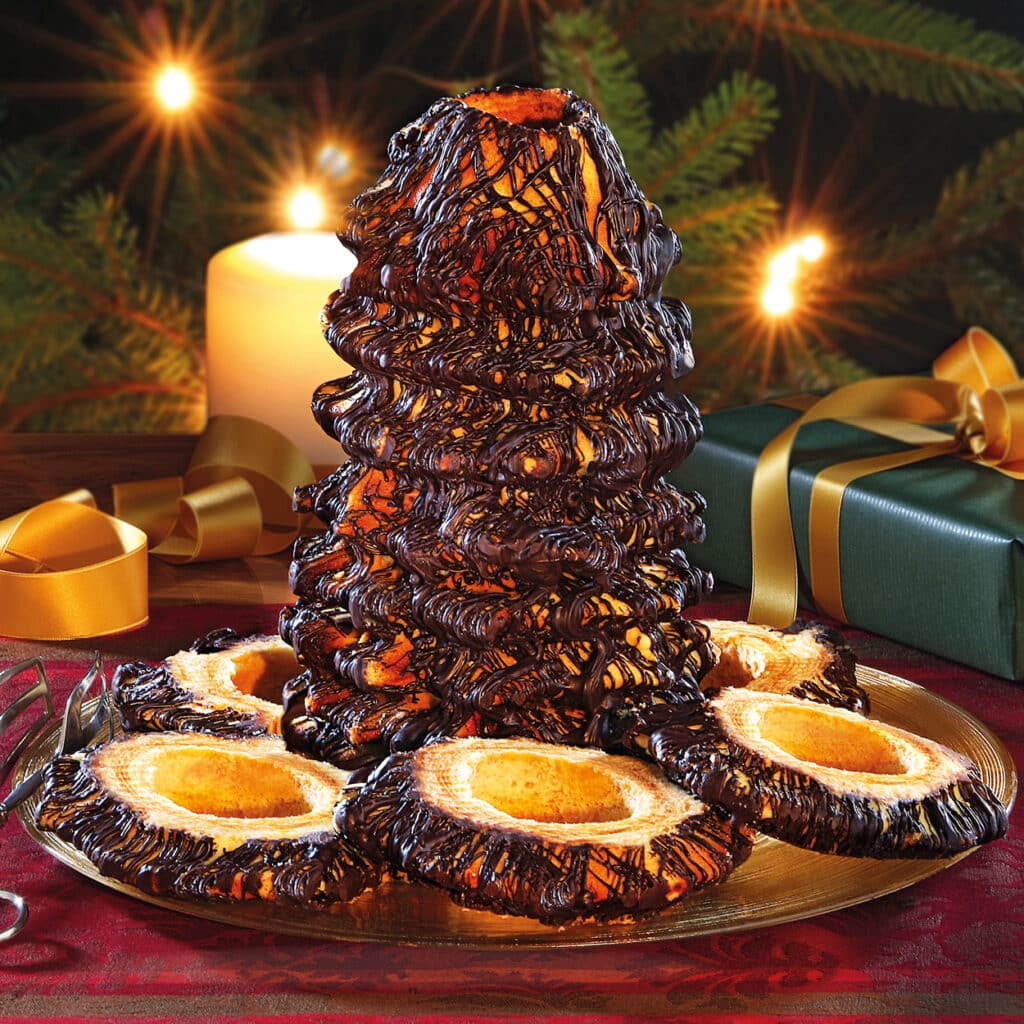 Baumkuchen mit dunklem Schokoladenüberzug in Tannenbaumform, serviert auf festlicher Platte mit Weihnachtsdeko