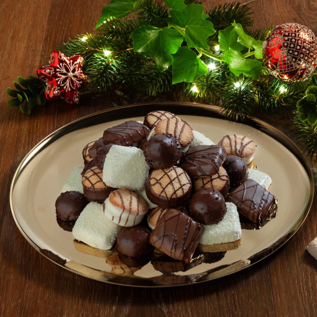 Bunte Mischung aus Schokoladenplätzchen und Pralinen auf goldener Platte, dekoriert mit Tannengrün und Weihnachtskugeln