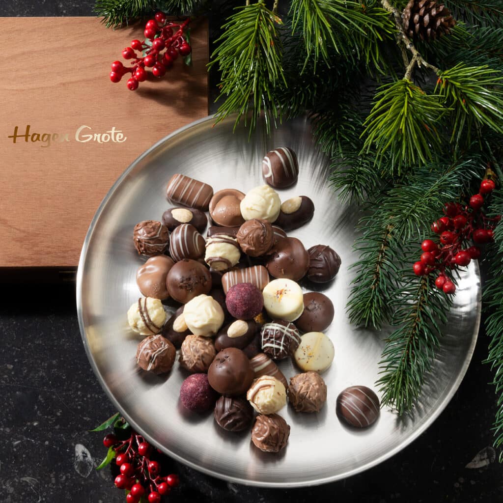 Pralinenmischung aus Schokolade, Trüffel und Mandeln in runder Schale, dekoriert mit Tannenzweigen und Beeren